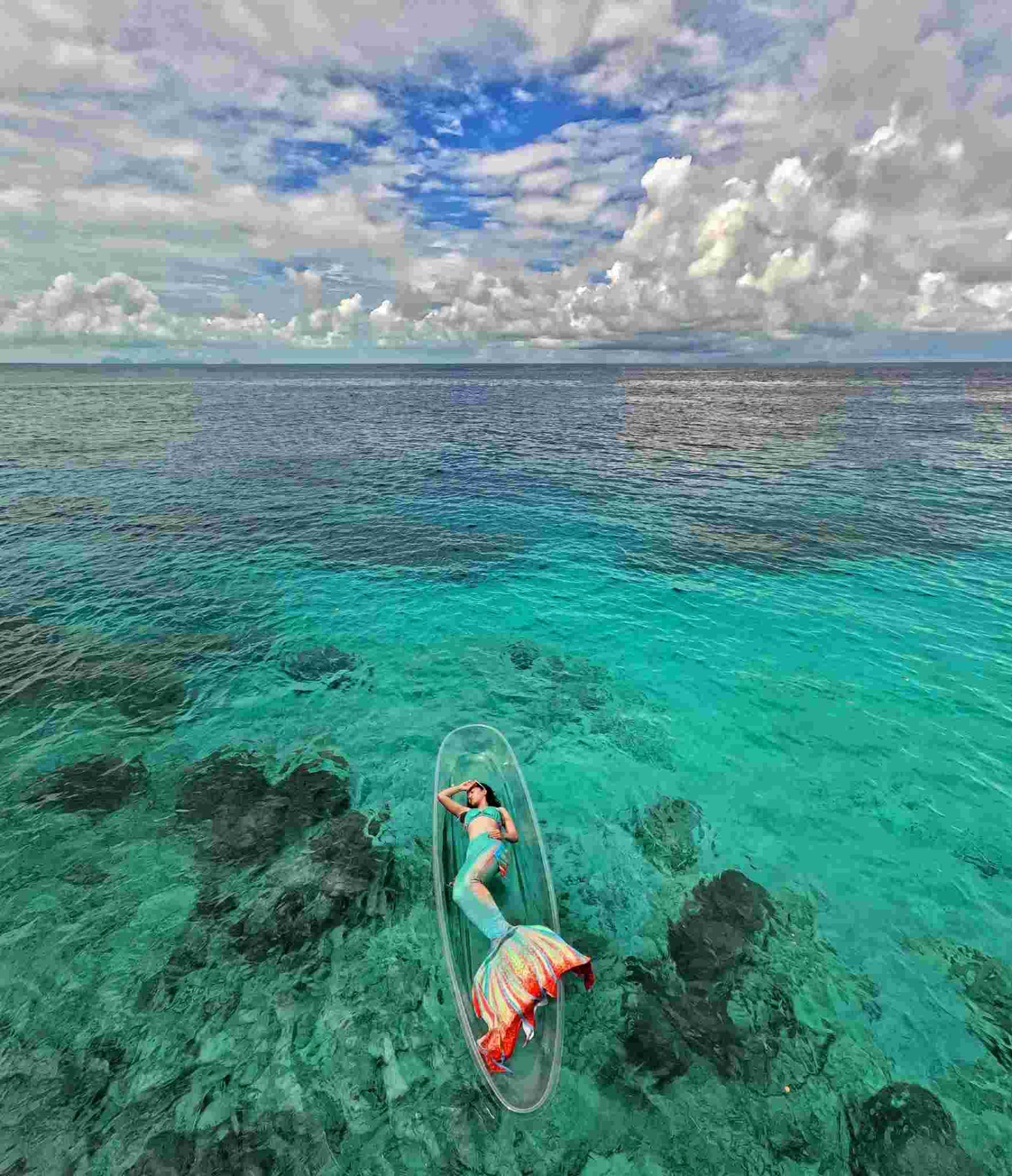 Angelia in her mermaid tail on a clear kayak over the ocean