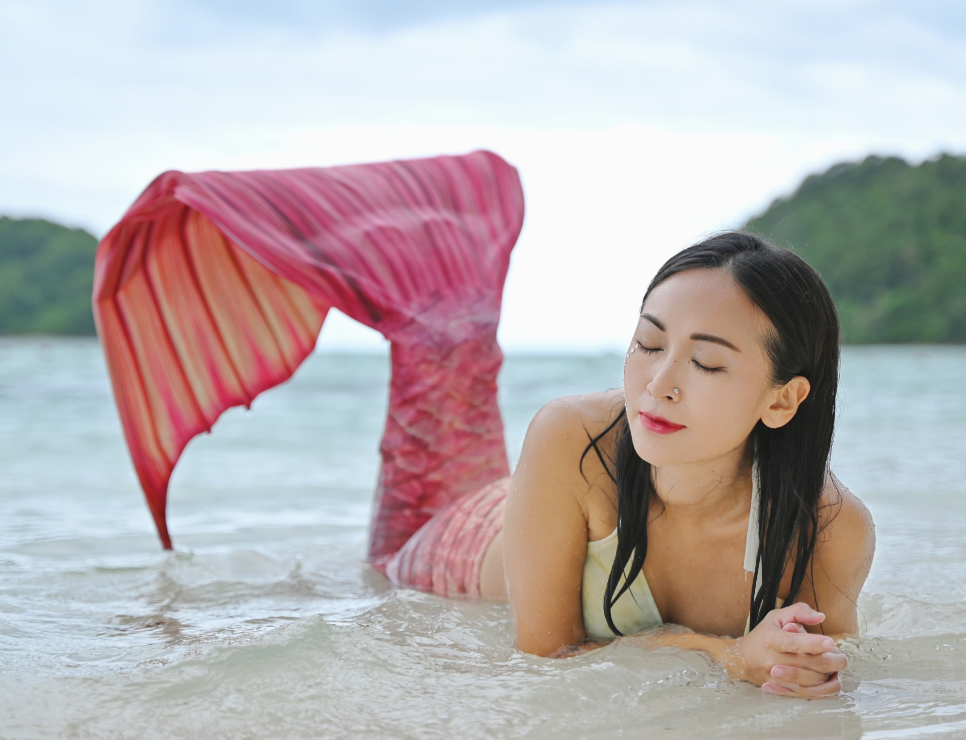 Angelia resting on the shore in a red mermaid tail