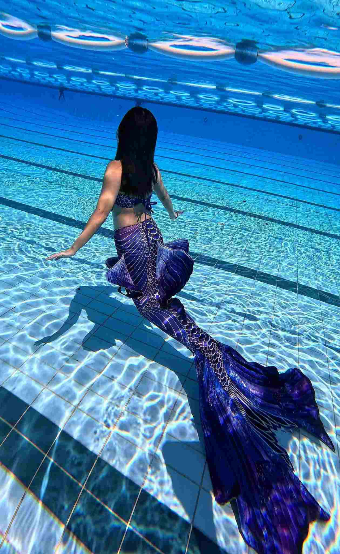 A mermaid in a purple tail gliding over the pool floor